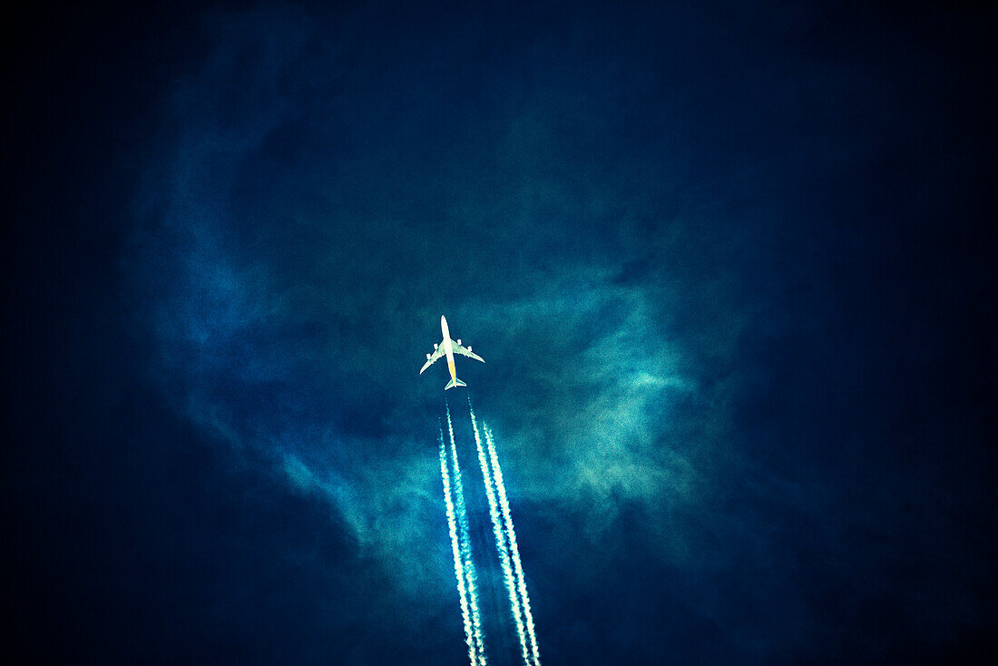 Verkehrsflugzeug mit Kondensstreifen am dunklen Himmel