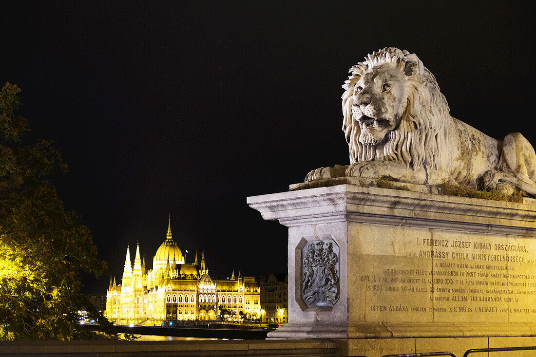 Lion Statue at Szechenyi Chain Bridge with Hungarian Parliament Building in the background, Budapest, Hungary