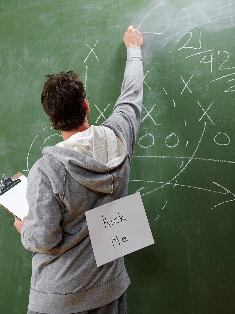 Man at Blackboard with Kick Me Sign on Back