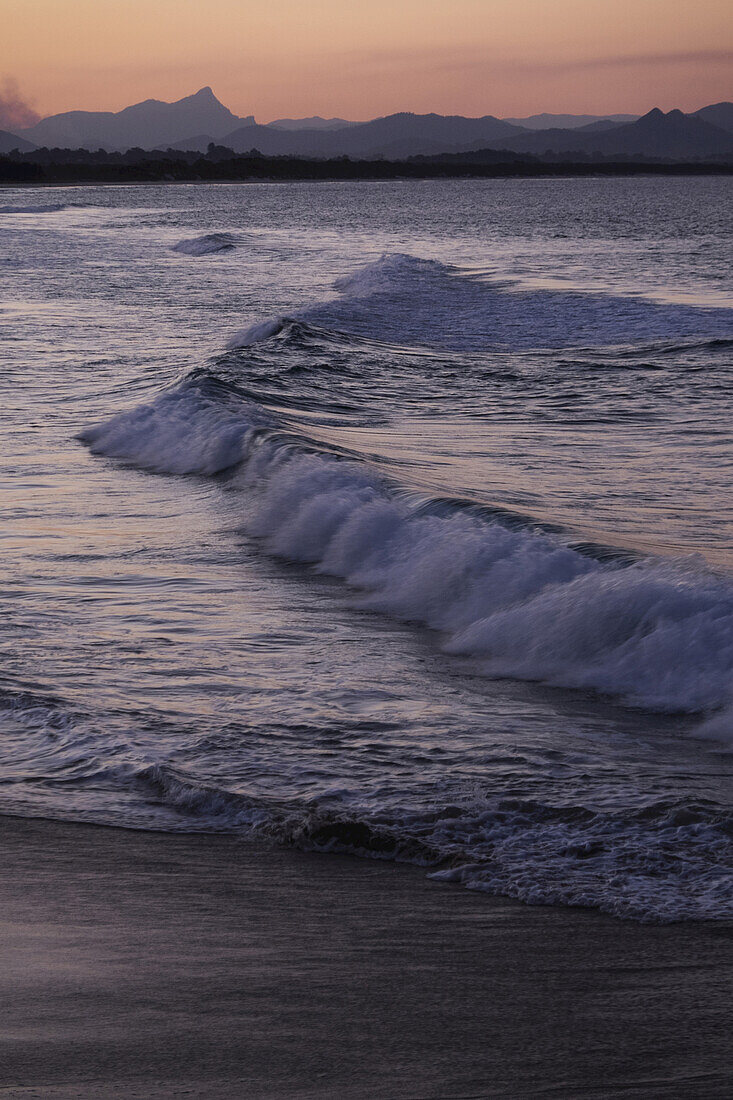 Wellen schlagen bei Sonnenuntergang an den Strand in Byron Bay in New South Wales, Australien