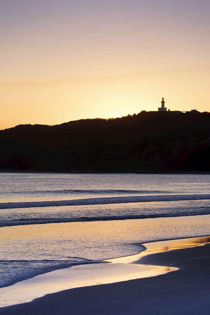 Silhouette des Cape Byron Lighthouse und sonnenbeschienener Strand bei Sonnenuntergang in Byron Bay in New South Wales, Australien