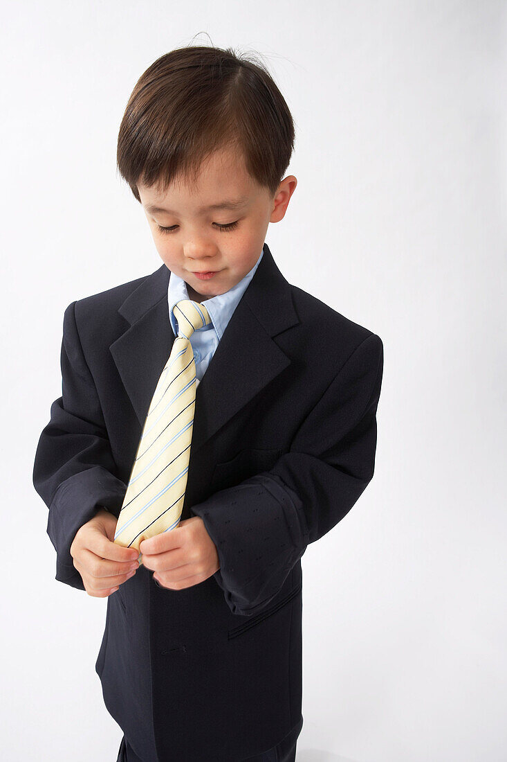 Kleiner Junge als Geschäftsmann verkleidet schaut auf seine Krawatte