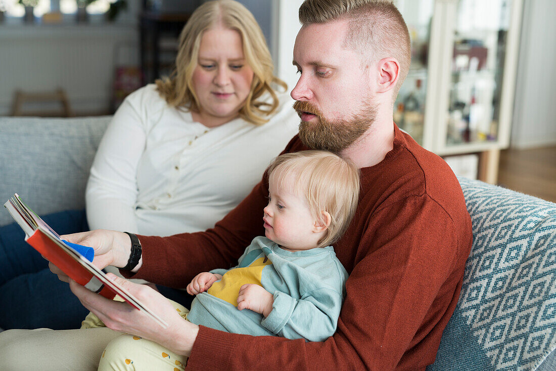Parents with baby with down syndrome reading on sofa