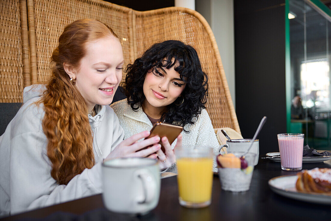 Smiling young women using phone in cafe