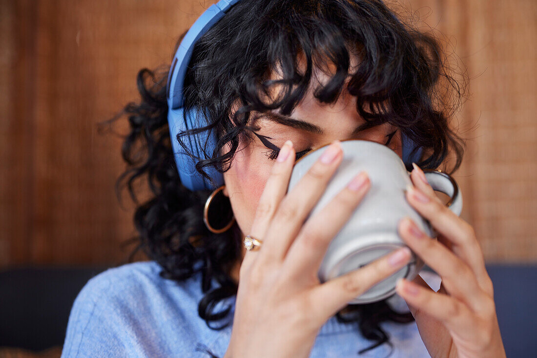 Junge Frau mit Kopfhörern trinkt Kaffee