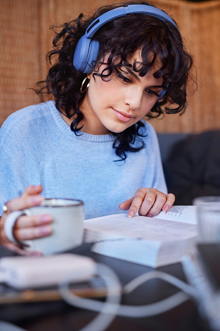 Junge Frau mit dunklen, lockigen Haaren und Kopfhörern beim Lesen eines Buches