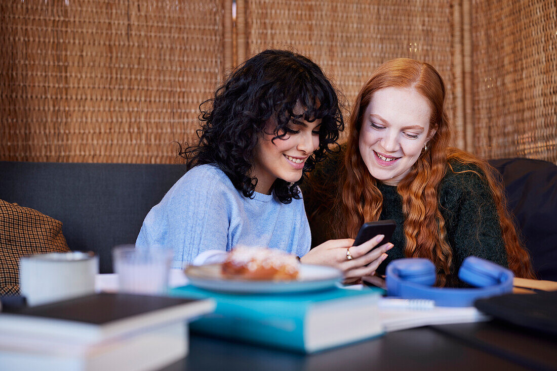 Lächelnde junge Frauen, die mit ihrem Handy auf soziale Medien schauen