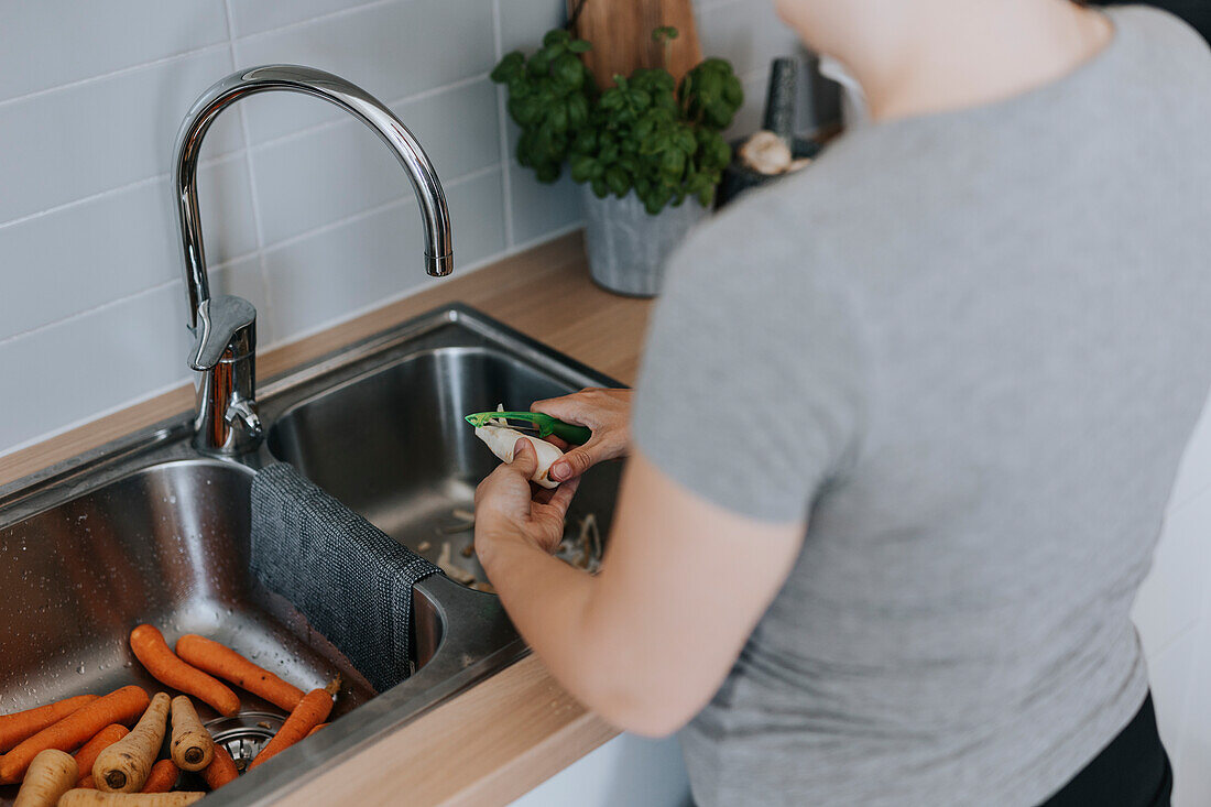 Woman peeling vegetables over kitchen sink
