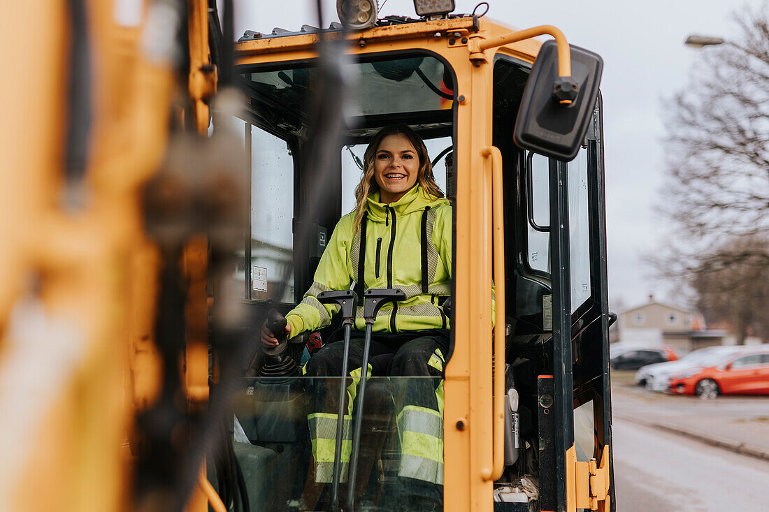Porträt einer lächelnden Straßenbauarbeiterin, die einen Bagger bedient