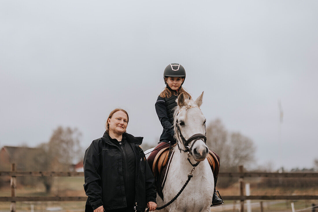 Girl horseback riding with female instructor looking at camera