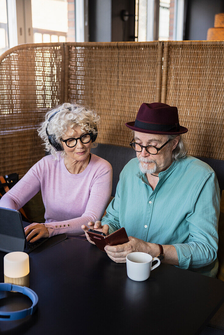 Senior couple sitting in cafe looking at cell phone