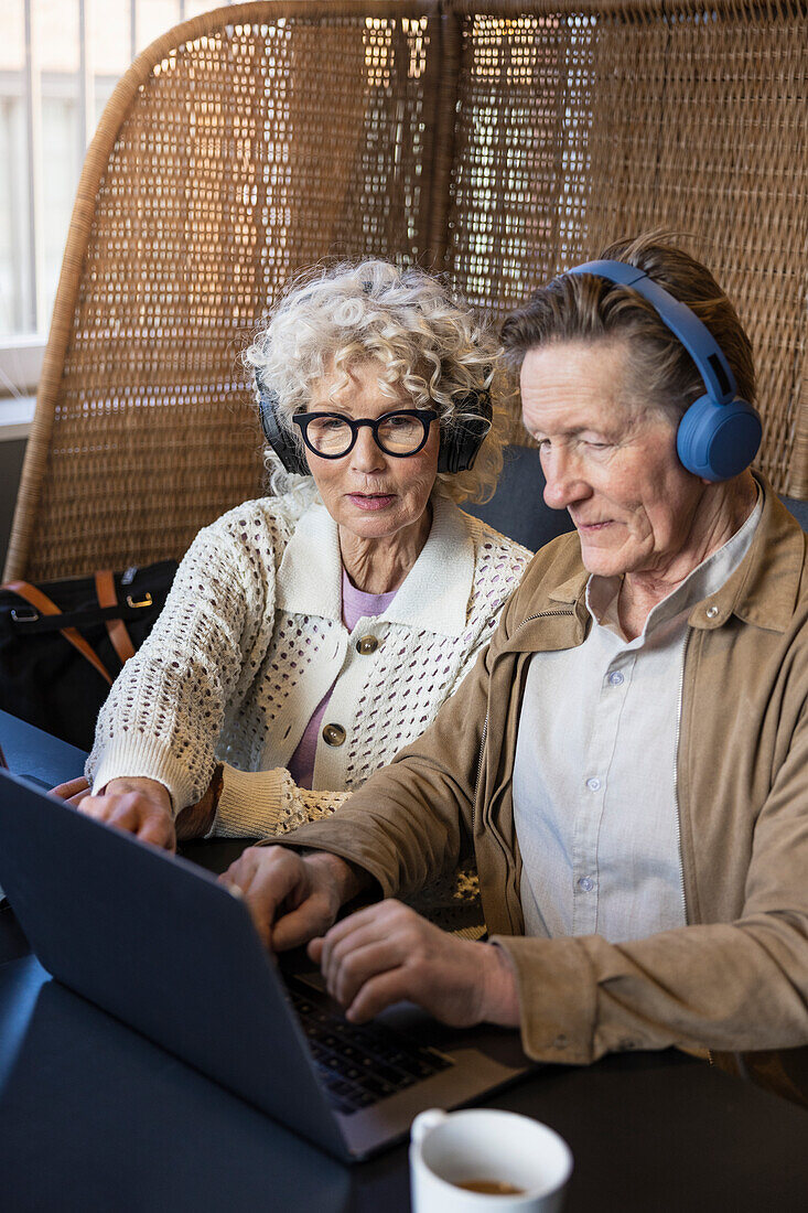 Senior couple sitting in cafe working on digital tablet and laptop