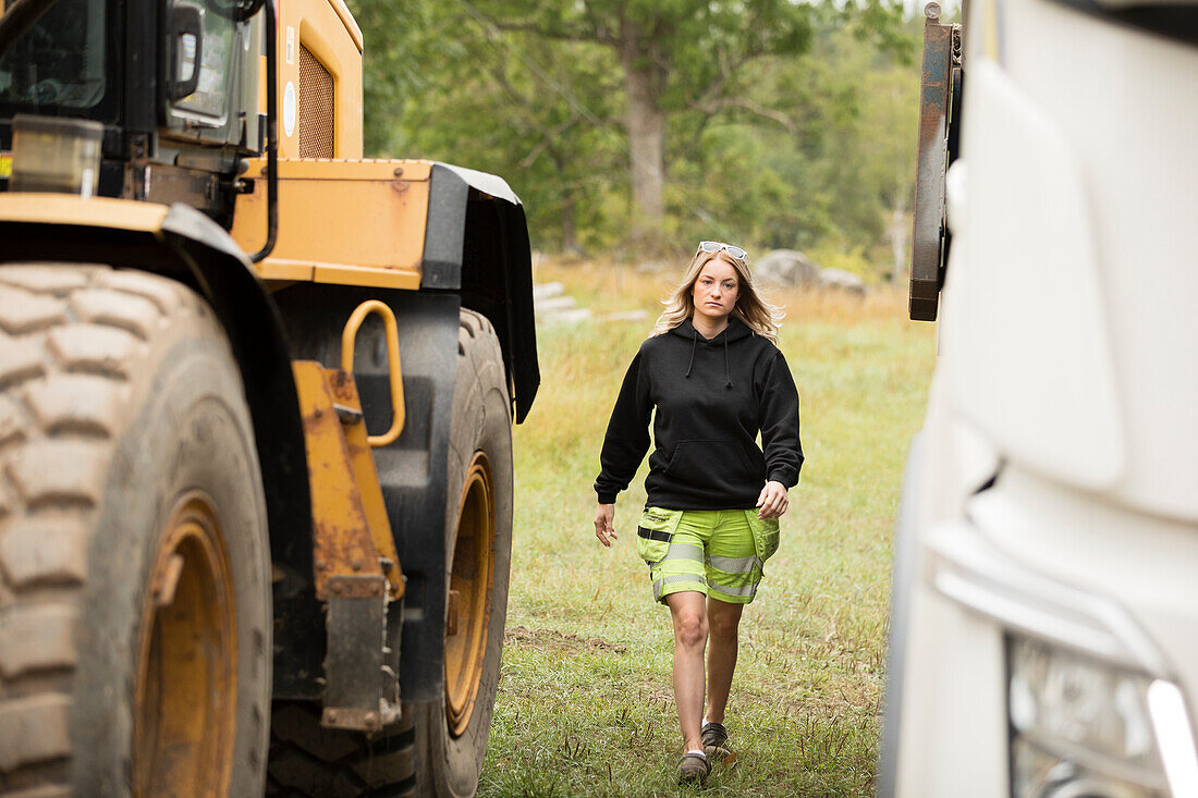 Young female construction worker walking next to excavator