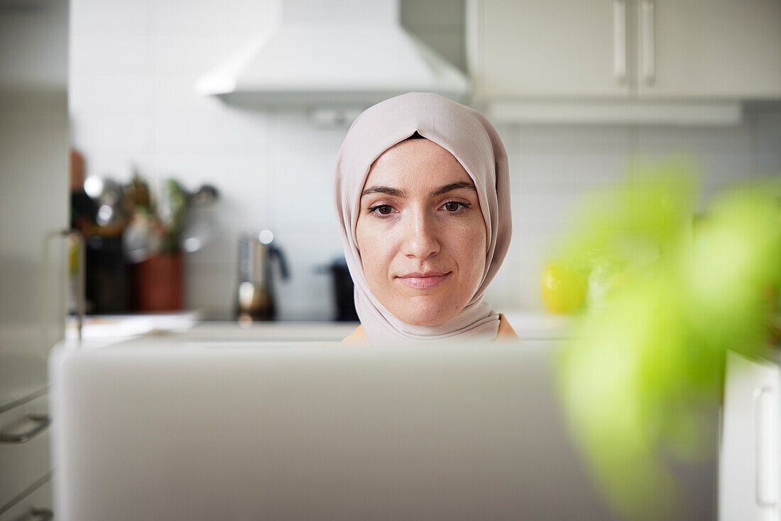 Lächelnde Frau mit Hidschab an einem Laptop
