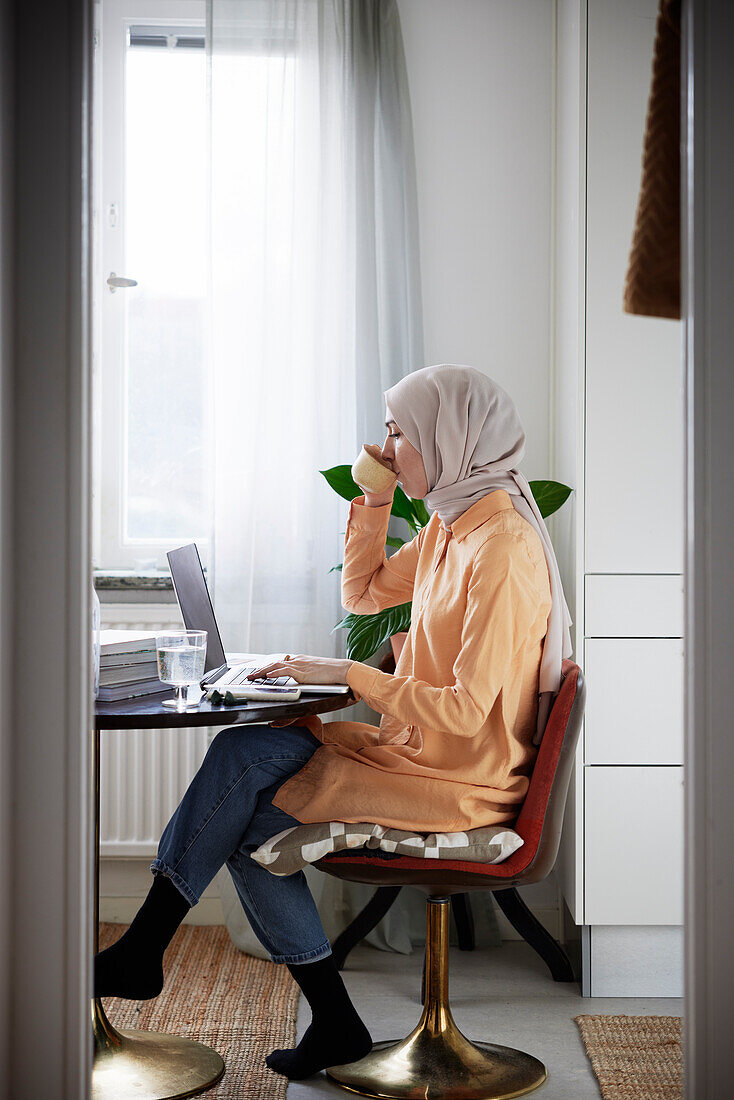 Ansicht einer Frau mit Hijab bei der Arbeit von zu Hause aus mit Laptop