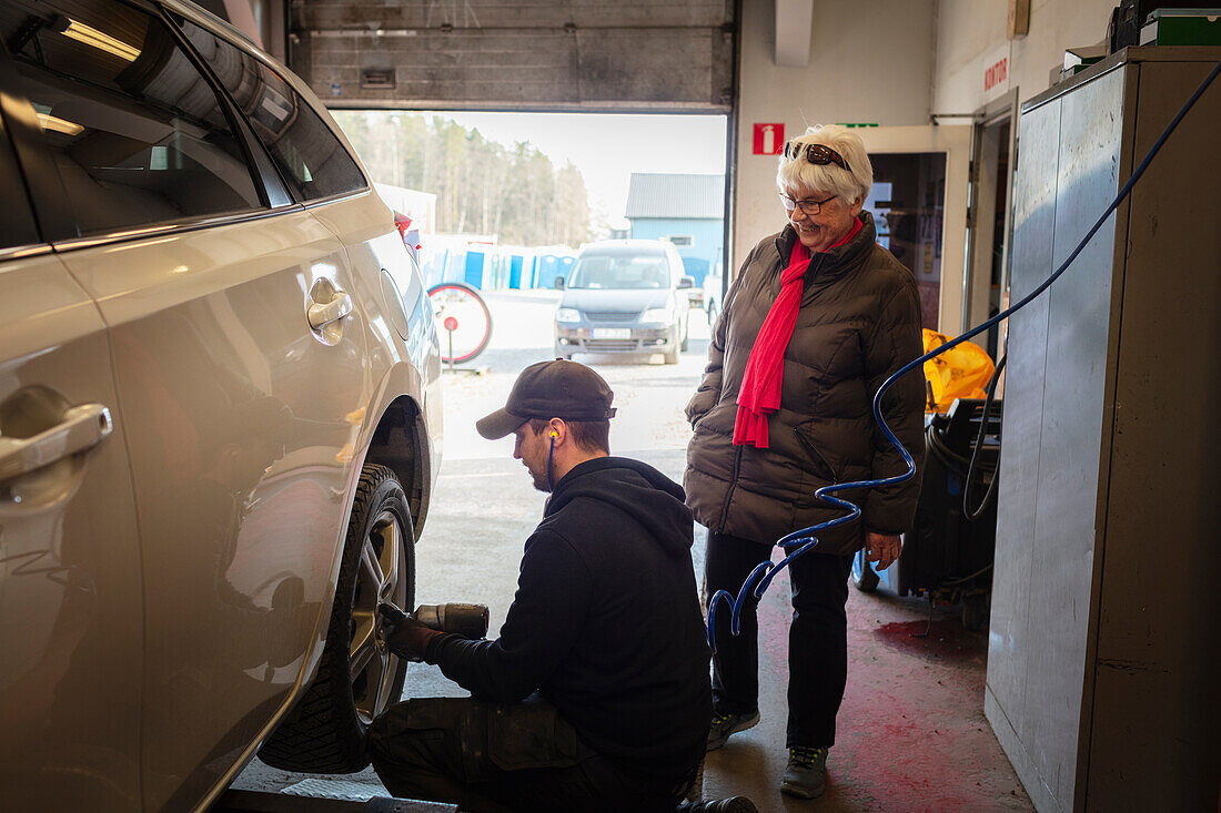 Mechanic in garage changing tires on car and talking to female client