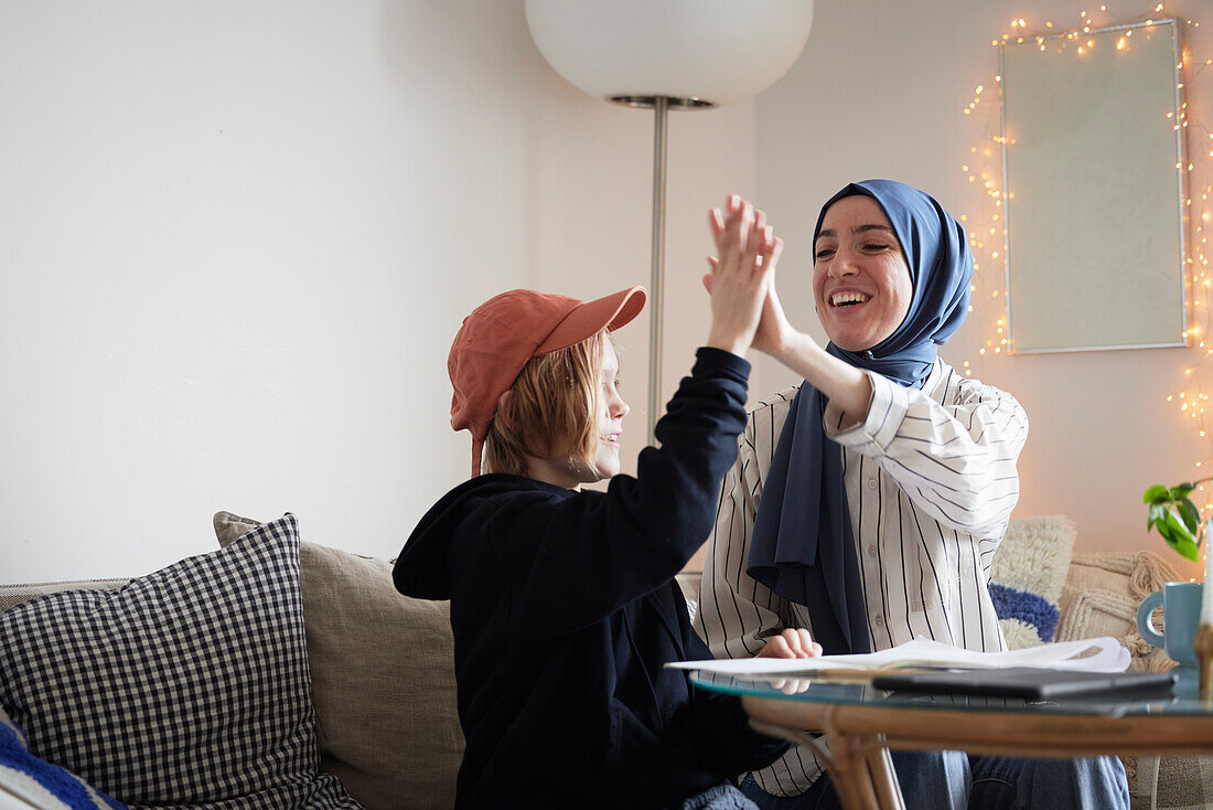 Hijab tragende Mutter hilft Sohn bei den Hausaufgaben und macht High Five
