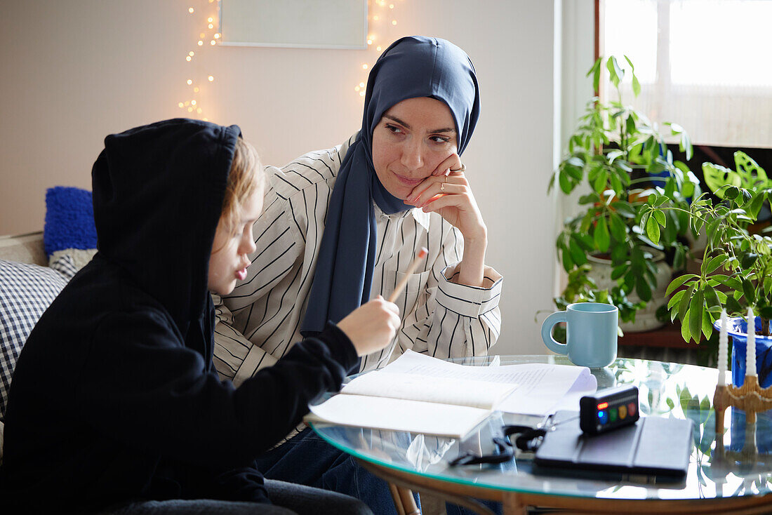 Mutter mit Hidschab hilft Sohn mit ADS oder ADHS bei den Hausaufgaben