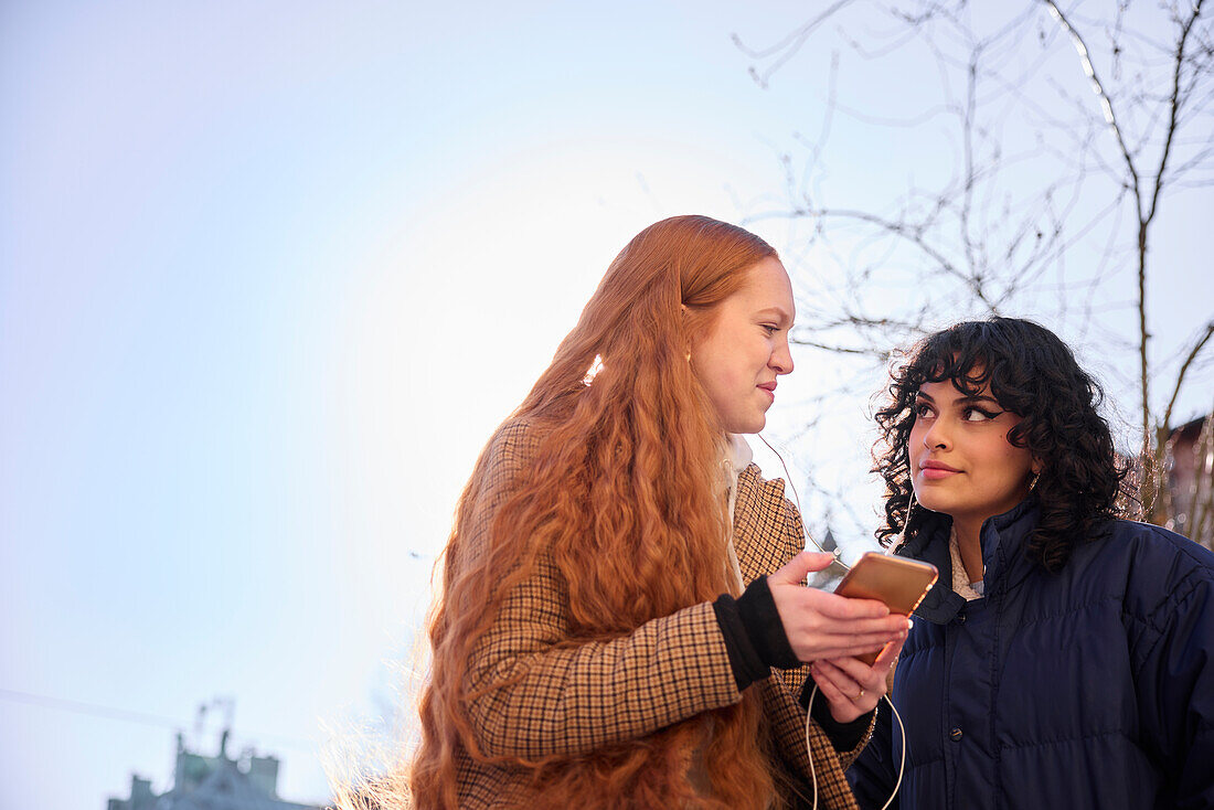 Female friends looking at cell phone outdoors with sun in the background