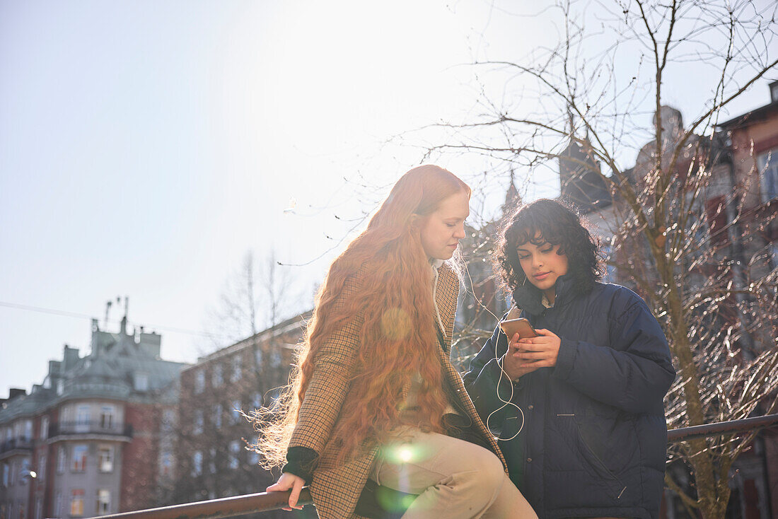 Female friends looking at cell phone outdoors with sun in the background