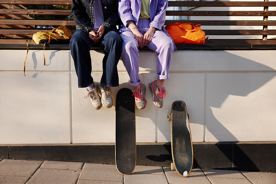 Low section of two women sitting near skateboards