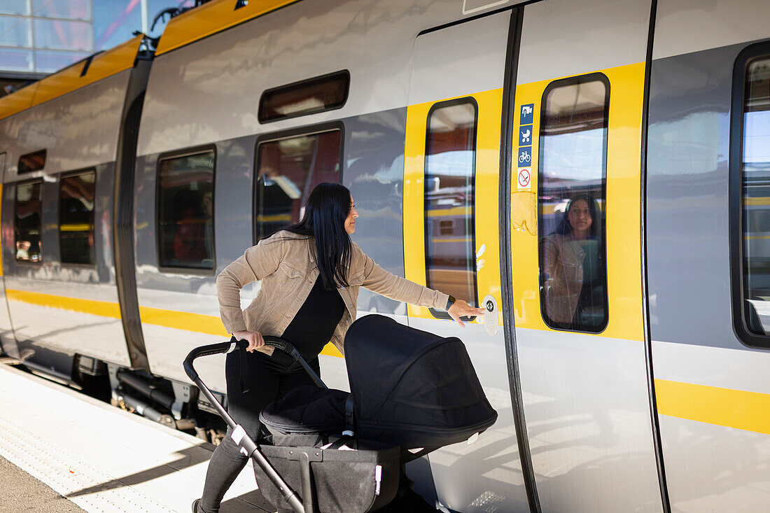 Mittlere erwachsene Frau am Bahnhof mit Kinderwagen beim Öffnen der Zugtür