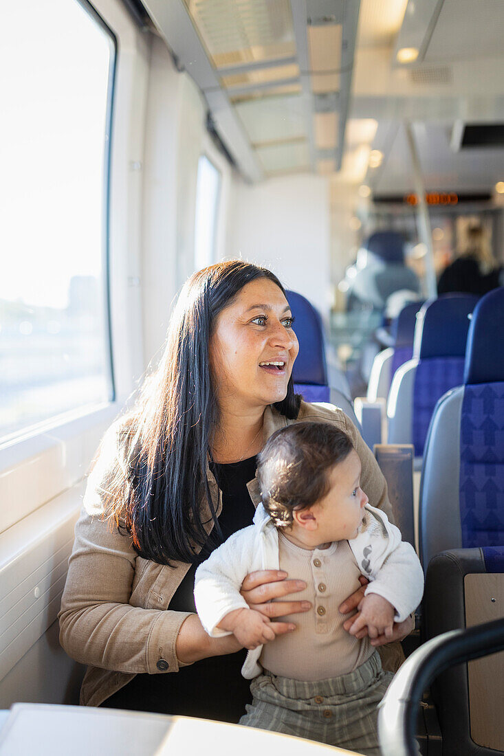 Smiling woman sitting in train with baby on her laps