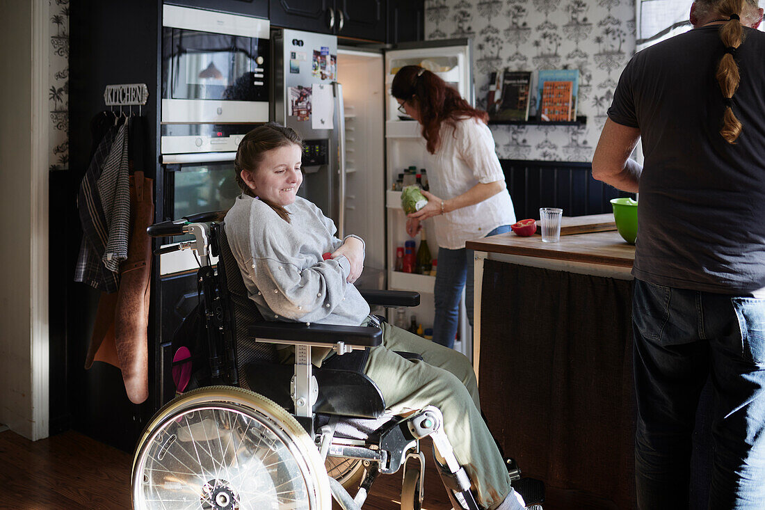 Parents with disabled daughter in wheelchair preparing food in kitchen