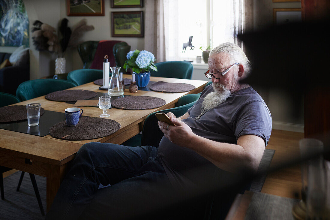 Mature man sitting at dining table and using cell phone