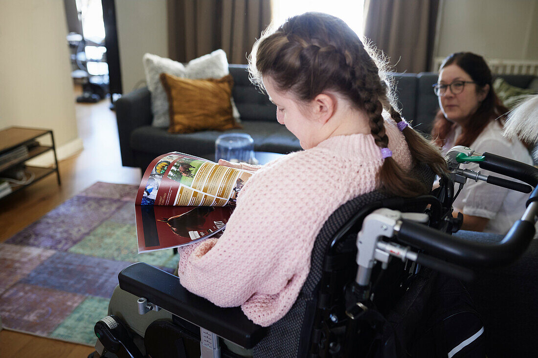 Disabled girl in living room reading magazine