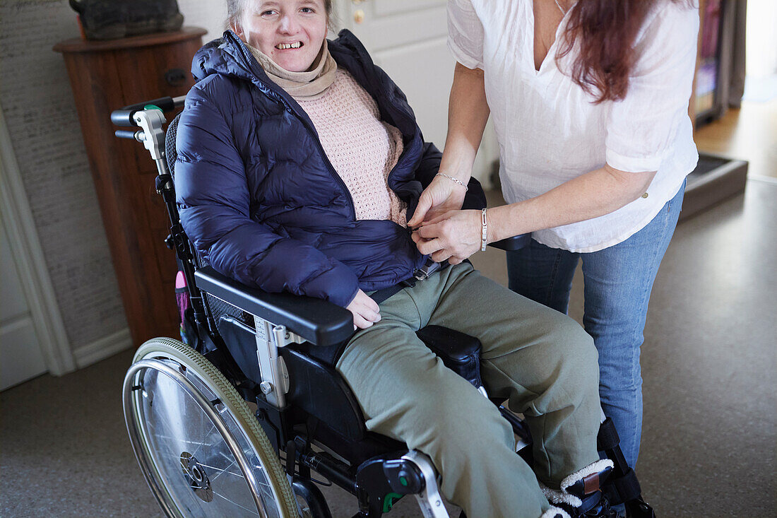 Mutter hilft behinderter Tochter im Rollstuhl beim Anziehen des Mantels