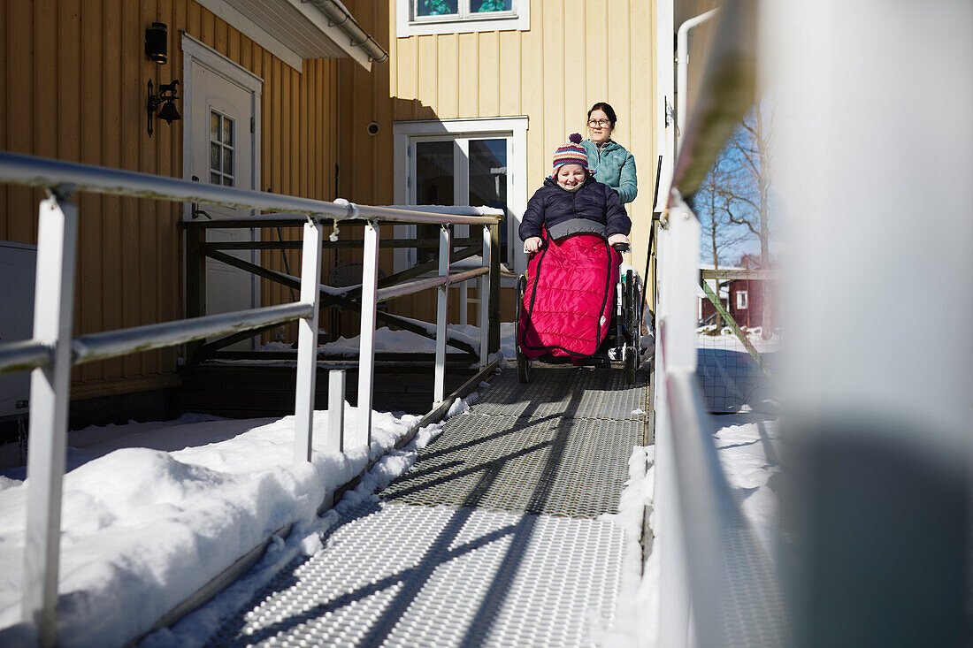 Mutter schiebt jugendliche Tochter im Rollstuhl bei Winterspaziergang