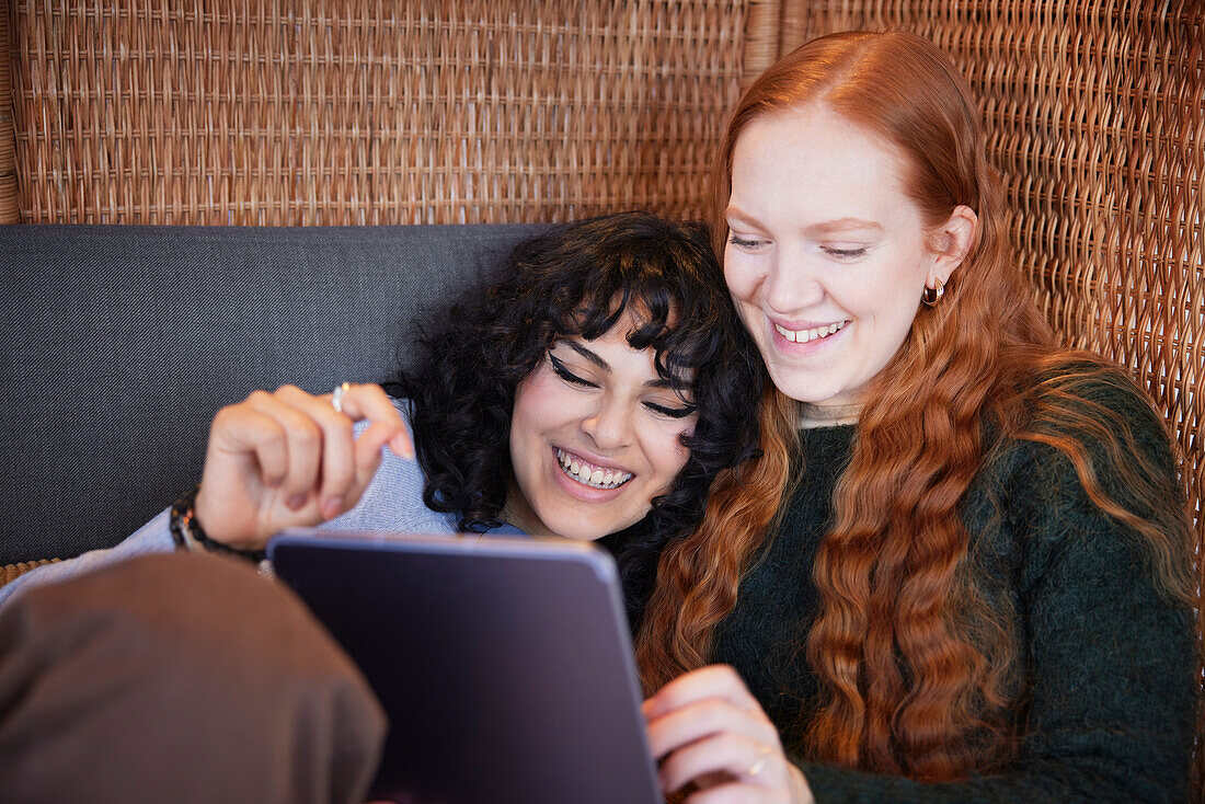 Smiling female friends scrolling social media or looking at tv show on digital tablet together