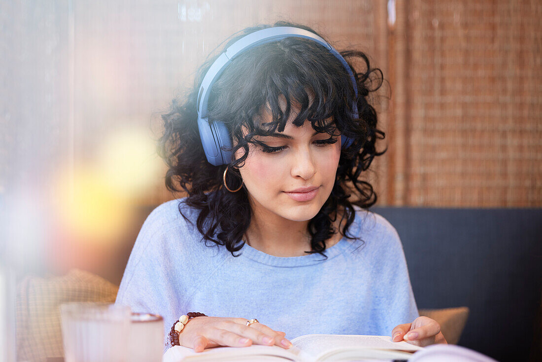 Junge Frau mit Kopfhörern hört Musik oder Podcast und liest ein Buch