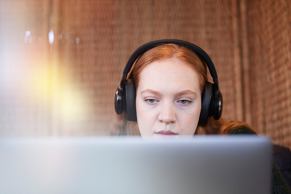 Young woman wearing headphones listening to music or podcast while studying using laptop