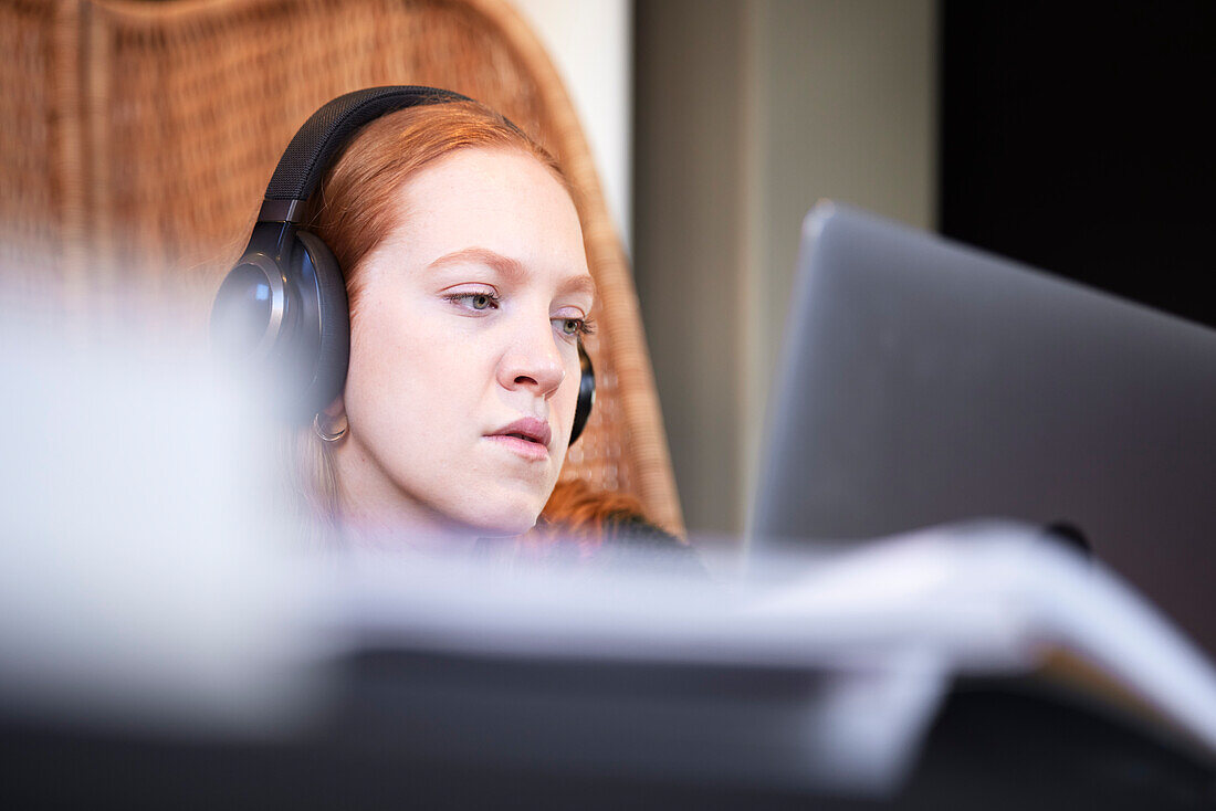 Young woman wearing headphones listening to music or podcast while studying using laptop