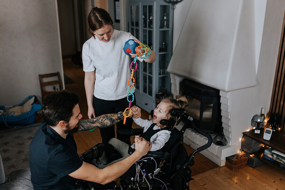 Eltern spielen mit lächelndem behindertem Kind im Rollstuhl