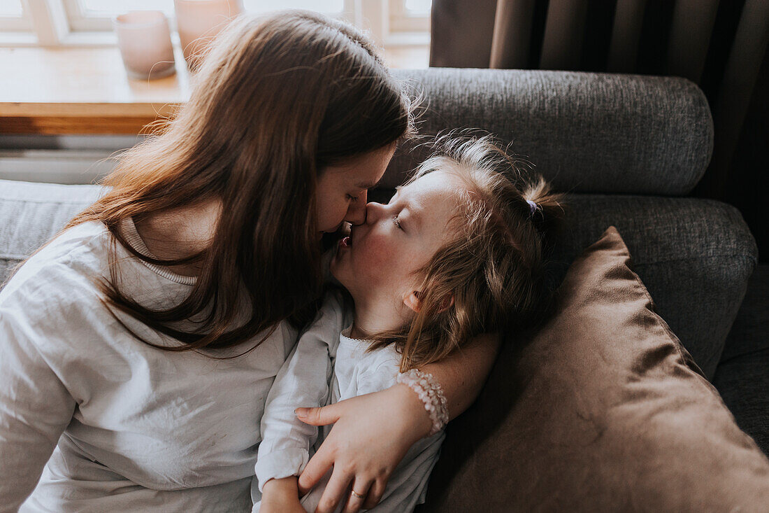 Mutter umarmt und küsst behindertes Kind auf Sofa