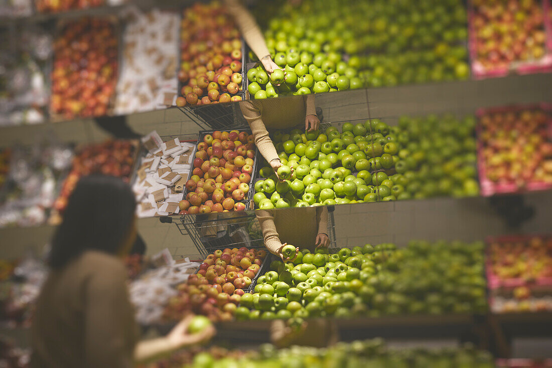 Frau beim Aussuchen von Äpfeln, Früchte spiegeln sich in Supermarkt-Spiegeln