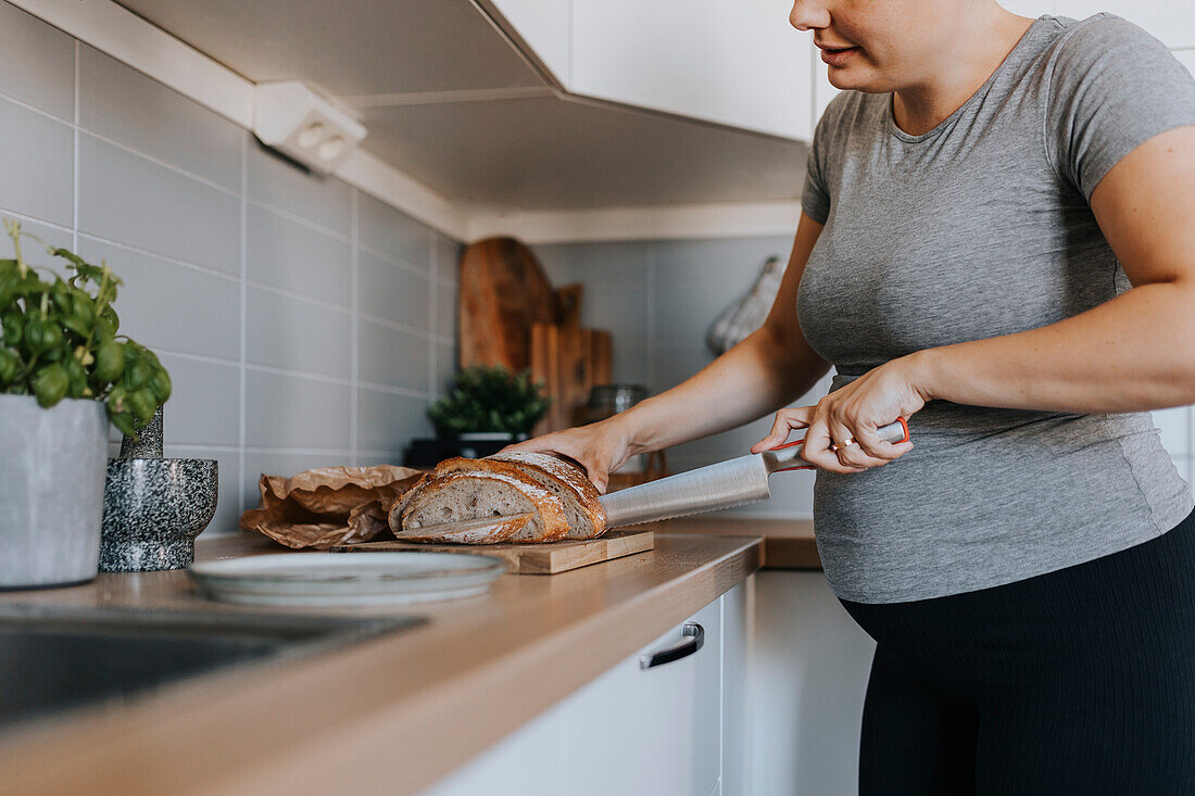 Pregnant woman slicing bread to prepare meal
