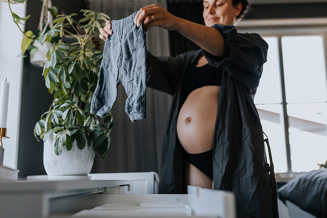 Schwangere Frau sortiert Babykleidung und bereitet sich auf die Ankunft des Babys vor