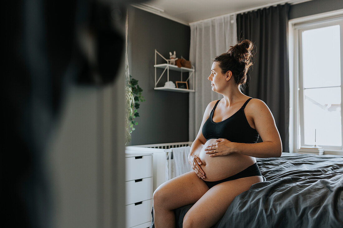 Schwangere Frau entspannt sich im Schlafzimmer und berührt ihren Bauch