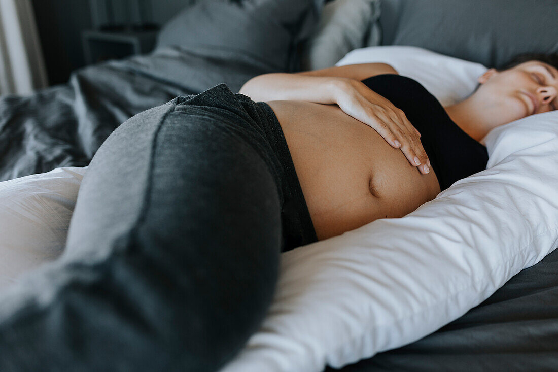Schwangere Frau schläft auf einem Schwangerschaftskissen im Bett
