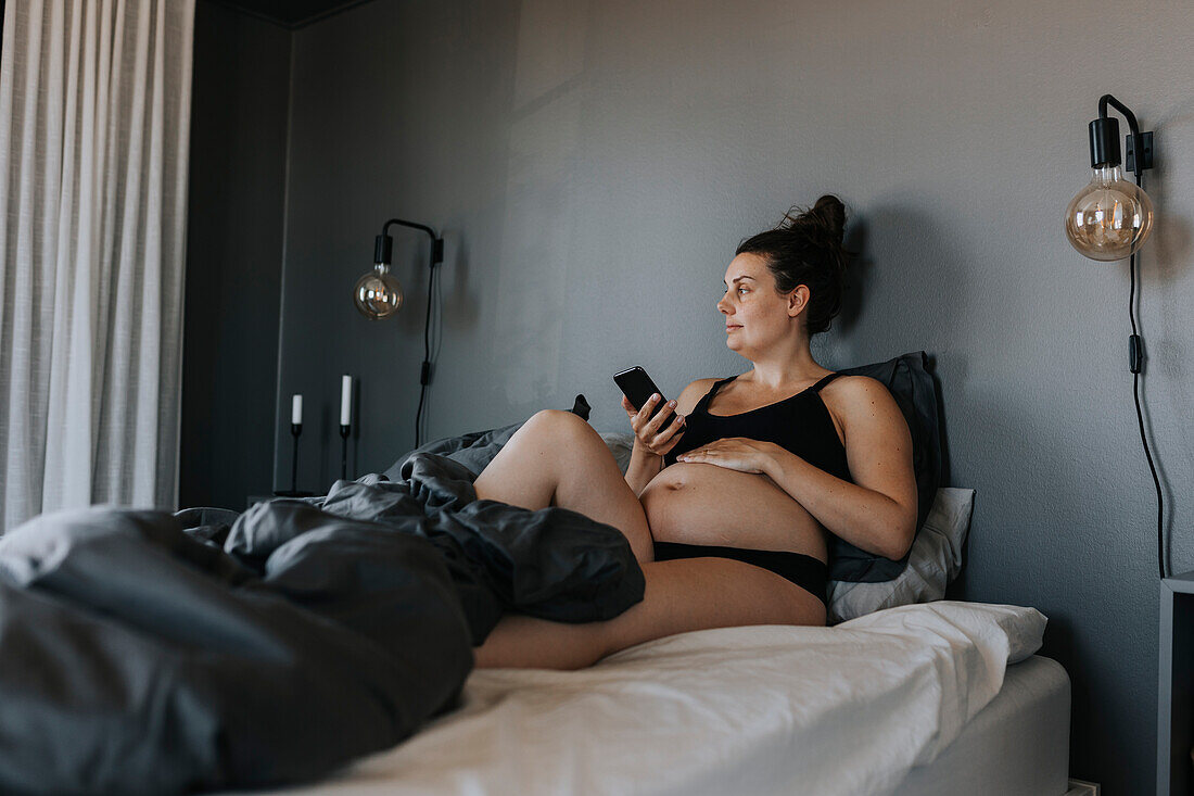 Schwangere Frau entspannt im Bett und telefoniert