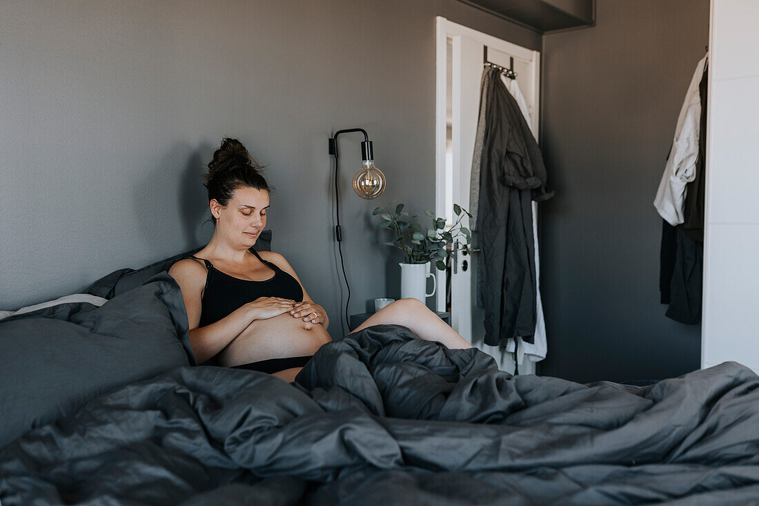 Schwangere Frau entspannt im Bett und berührt vorsichtig ihren Bauch