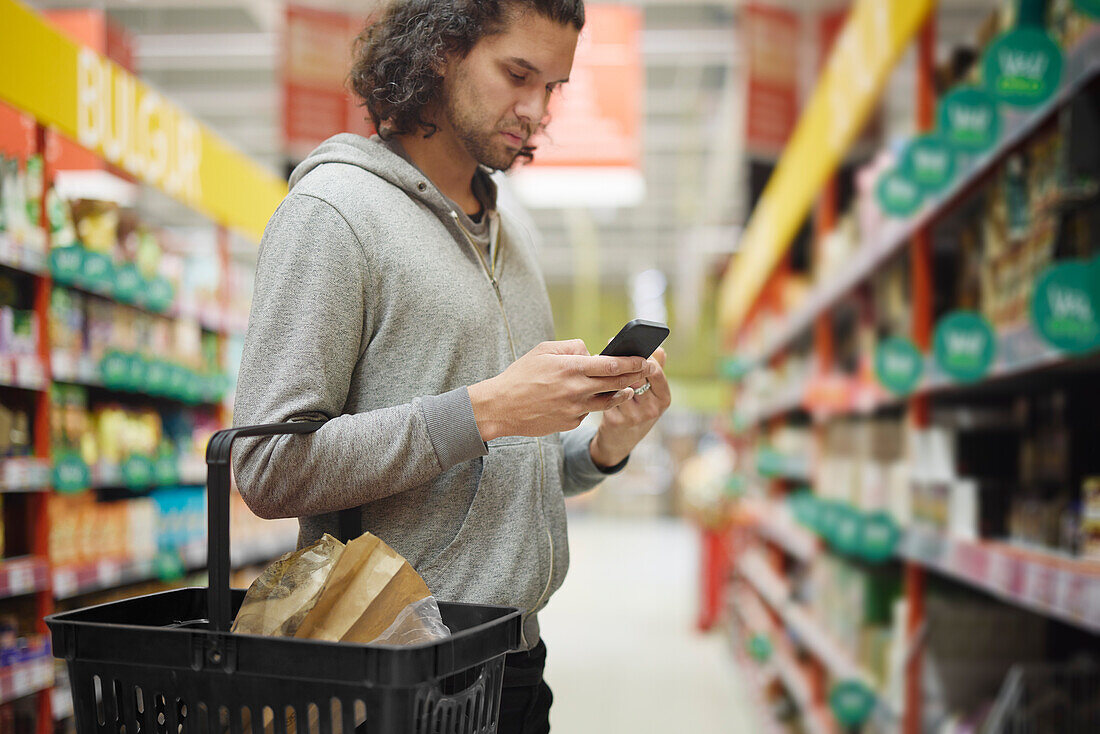 Mann im Supermarkt vergleicht Preise während der Inflation auf dem Handy
