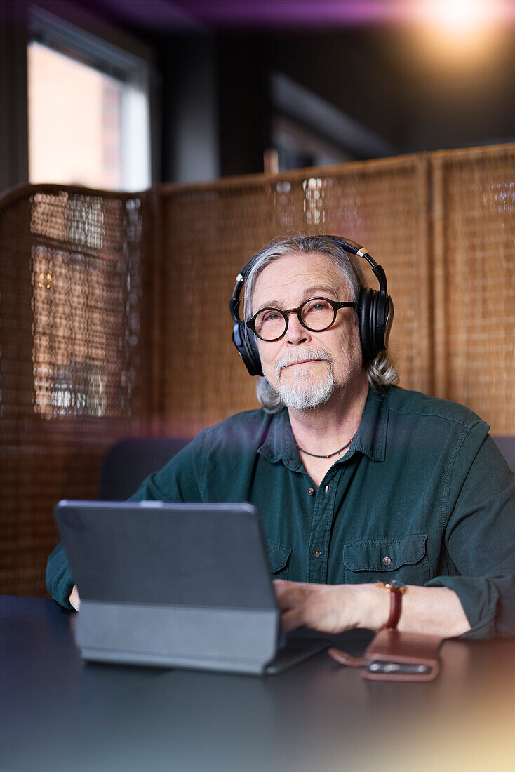 Portrait eines älteren Mannes mit Kopfhörern und Tablet