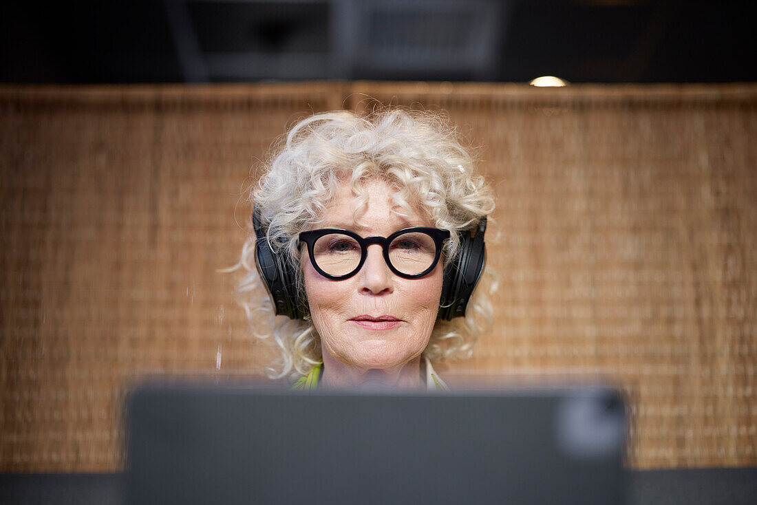 Ältere Frau mit Kopfhörern am Tablet