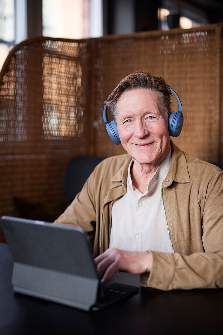 Portrait eines älteren Mannes mit Kopfhörern und Tablet