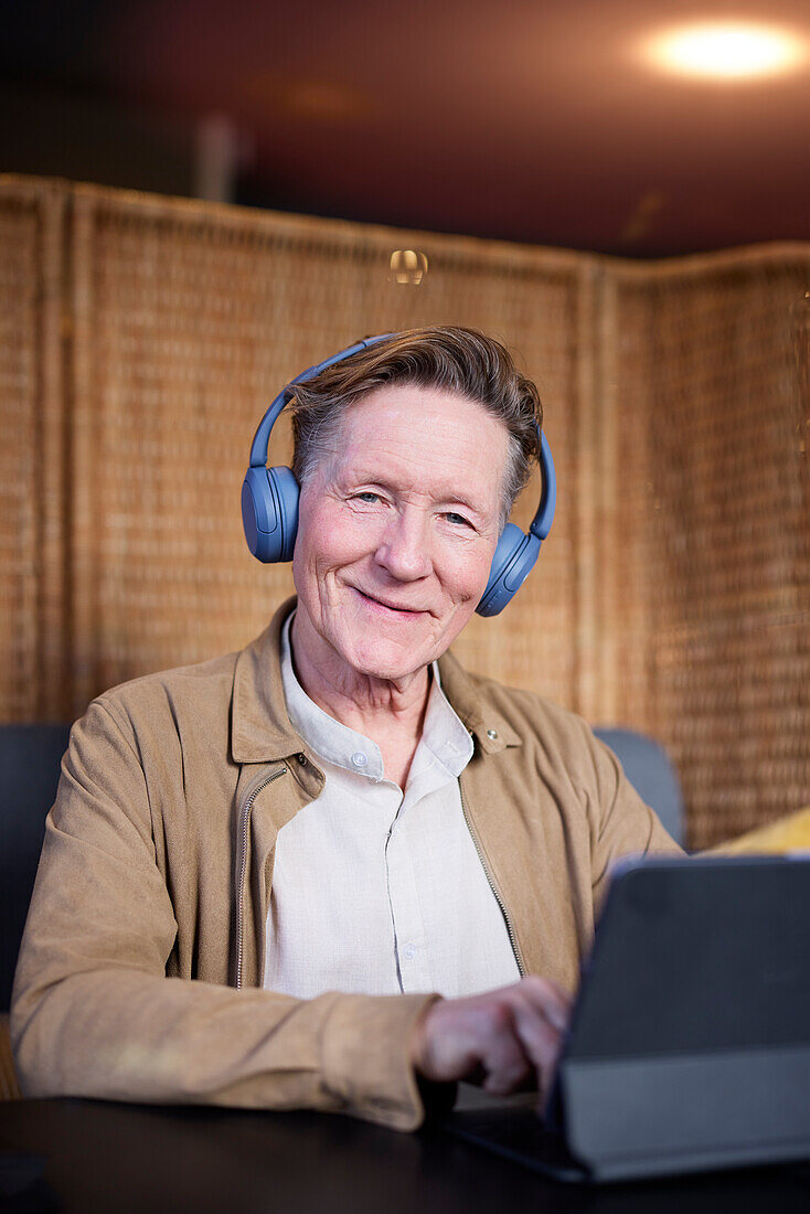 Porträt eines älteren Mannes mit Kopfhörern, der ein Tablet benutzt